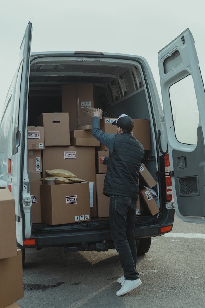 A courier organizing boxes in a delivery van for shipment on a cloudy day.