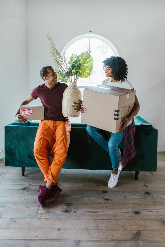 Cheerful couple sitting on a couch holding moving boxes, symbolizing new beginnings.